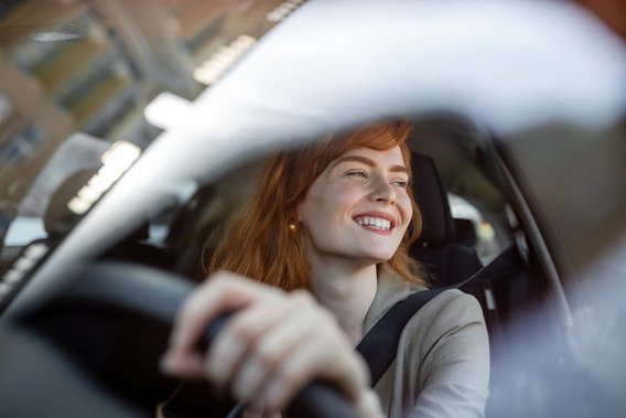 Abstinenznachweis für die MPU bei TÜV NORD Lächelnde Frau am Steuer eines Autos, aufgenommen durch die Windschutzscheibe