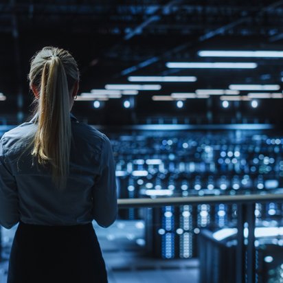 Person steht in einem großen, beleuchteten Serverraum und blickt auf die Reihen von Servern.