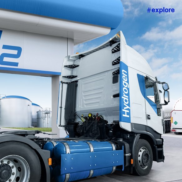 Wasserstoff-LKW an Tankstelle Ein moderner Wasserstoff-LKW steht an einer Wasserstofftankstelle. Der LKW ist mit großen Wasserstofftanks ausgestattet. Im Hintergrund sind weitere Tanks und ein klarer blauer Himmel zu sehen.