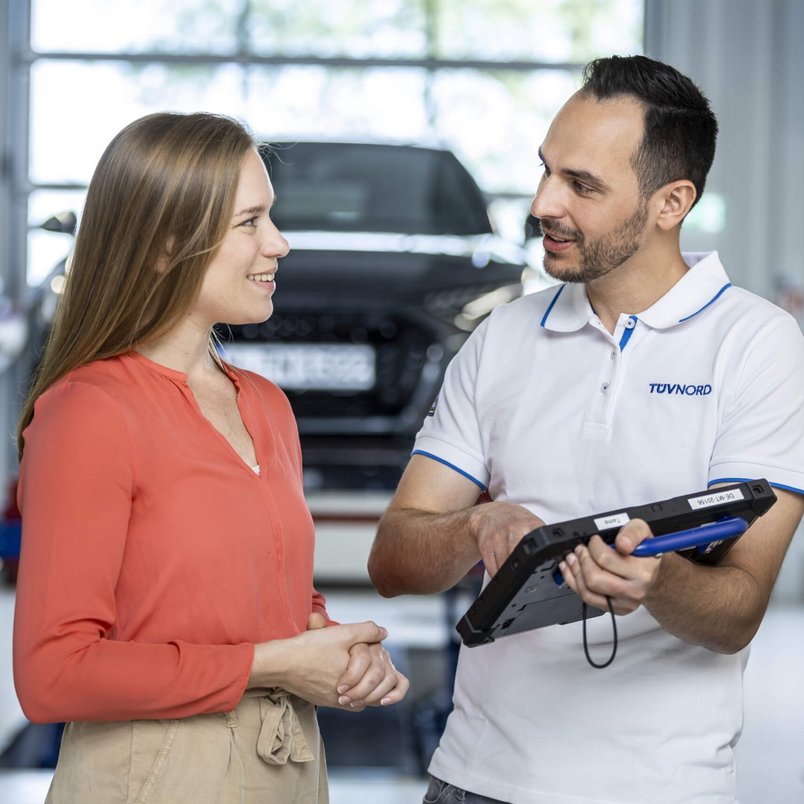 Beratungsgespräch bei TÜV NORD Mobilität in der TÜV NORD Station TÜV NORD Mitarbeiter im Gespräch mit einer Kundin in einer Prüfhalle
