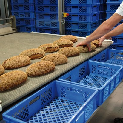 Industrielle Brotfertigung Symbolbild ISO 22000 Zertifizierung - Hände eines Mitarbeitenden greifen Brote von einem Laufban