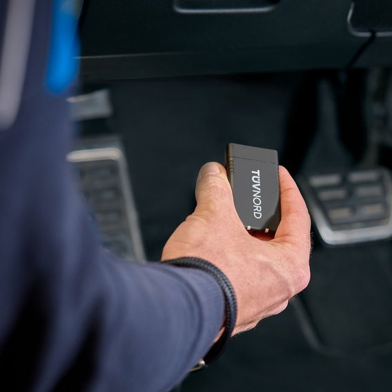 Fahrzeugdiagnose mit TÜV NORD Onboard Diagnose Prüfingenieur hält TÜV NORD Onboard Diagnose im Fahrzeug