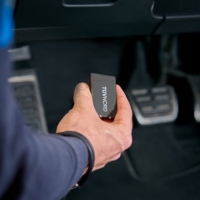 TÜV NORD Guardian Guardian Gerät in einer Hand vor den Pedalen eines Autos