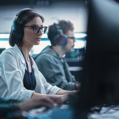 Personen arbeiten konzentriert an Computern in einem modernen Büro, tragen Headsets.