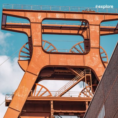 Ein orangefarbener Förderturm mit charakteristischen Stahlkonstruktionen vor einem klaren blauen Himmel, typisch für Bergbauanlagen im Ruhrgebiet.