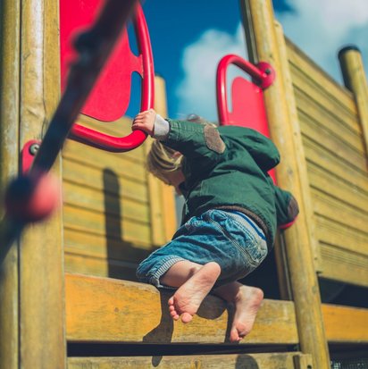 TUEV NORD-Spielplatzprüfung Ein Kind klettert barfuß auf ein Spielgerät.